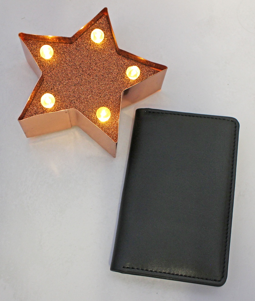 A star-shaped marquee light with five illuminated bulbs next to a closed black rectangular notebook.