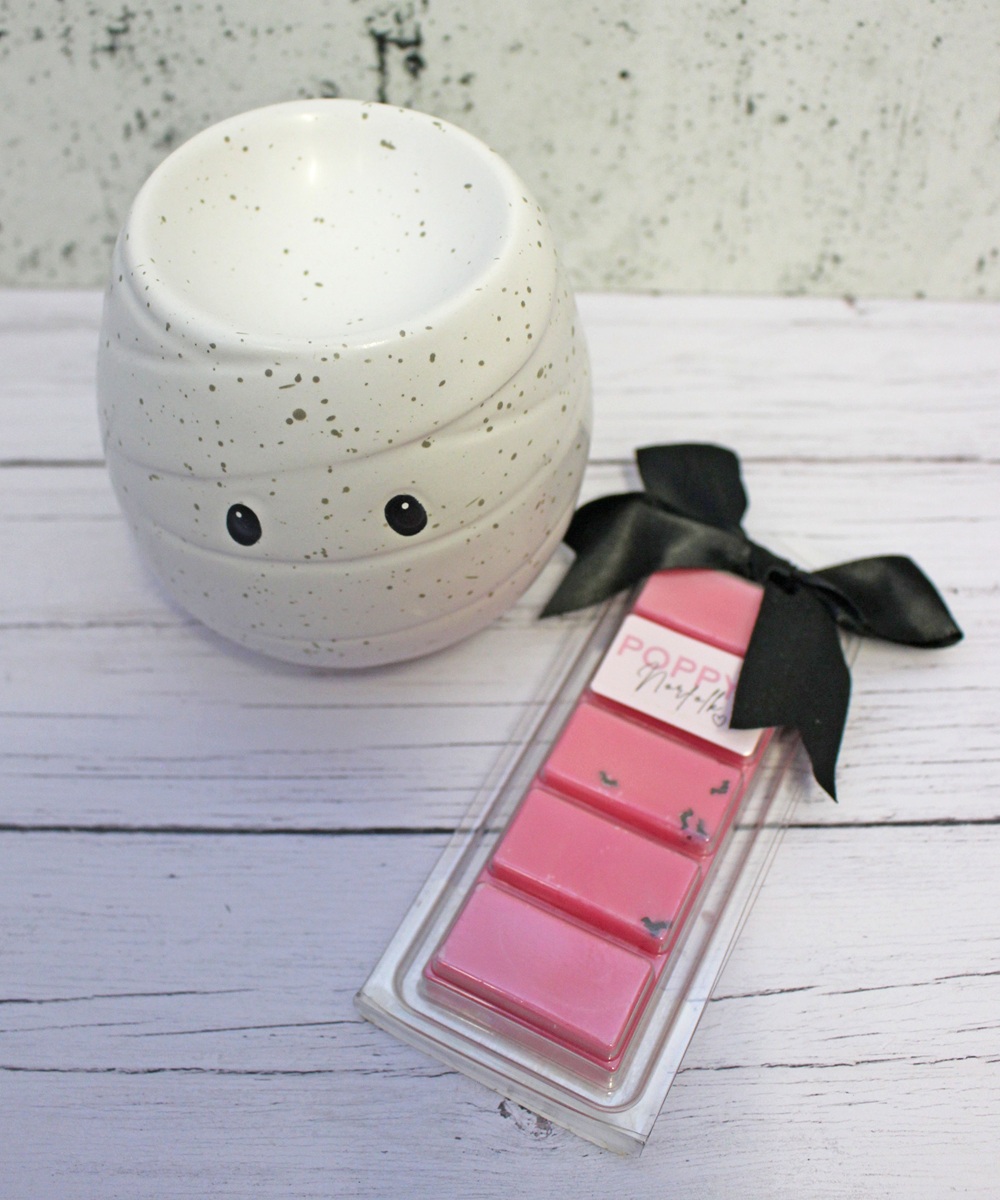 A white speckled mummy-shaped wax warmer next to a pink wax melt bar tied with a black ribbon.
