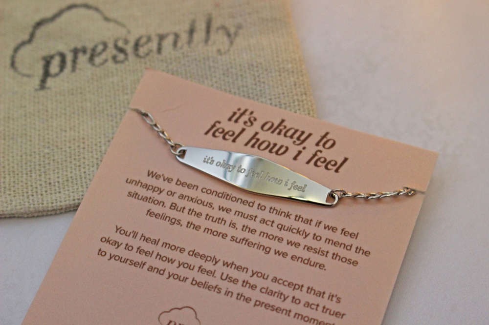A silver bar bracelet engraved with it's okay to feel how I feel pinned to a display card printed with the same phrase and an inspirational message.