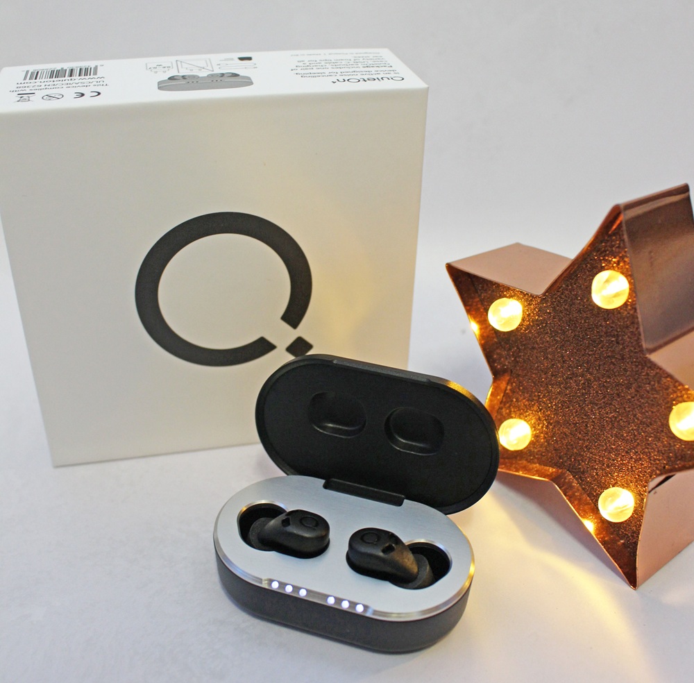 Black wireless earphones in an open charging case, placed in front of a white QuietOn product box and a decorative light-up star.