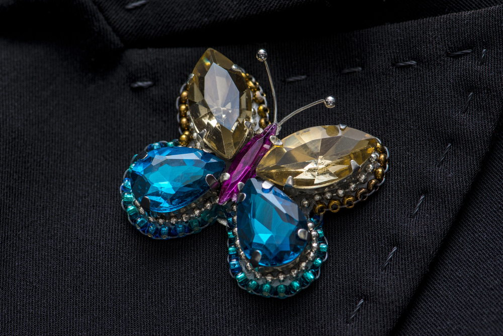 Butterfly brooch made of blue and gold crystals with a purple centre, pinned to a black fabric lapel.