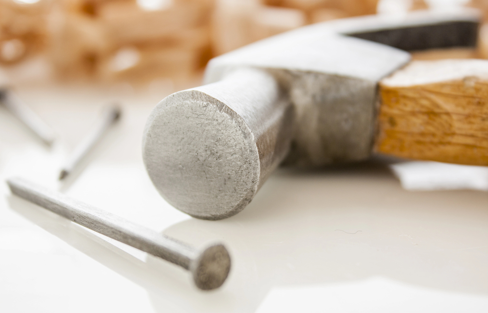 A hammer resting on a surface next to several nails.