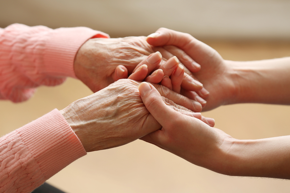 A younger person's hands gently holding the hands of an older person.