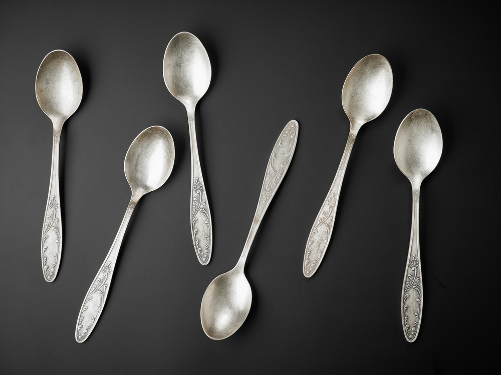 Six silver spoons with ornate handles arranged on a black background.