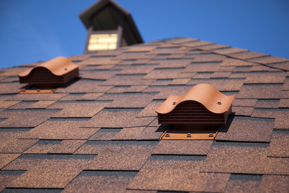 Two brown roof vents mounted on a tiled roof being prepared for replacing an old roof, set under a clear blue sky.