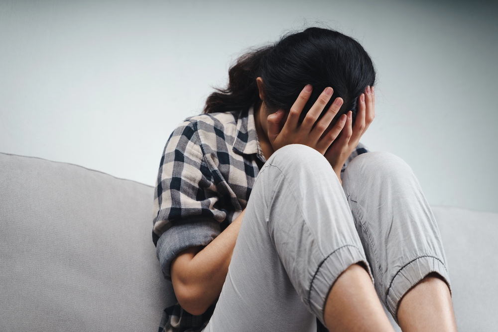 A person sitting on a settee with their head in their hands.