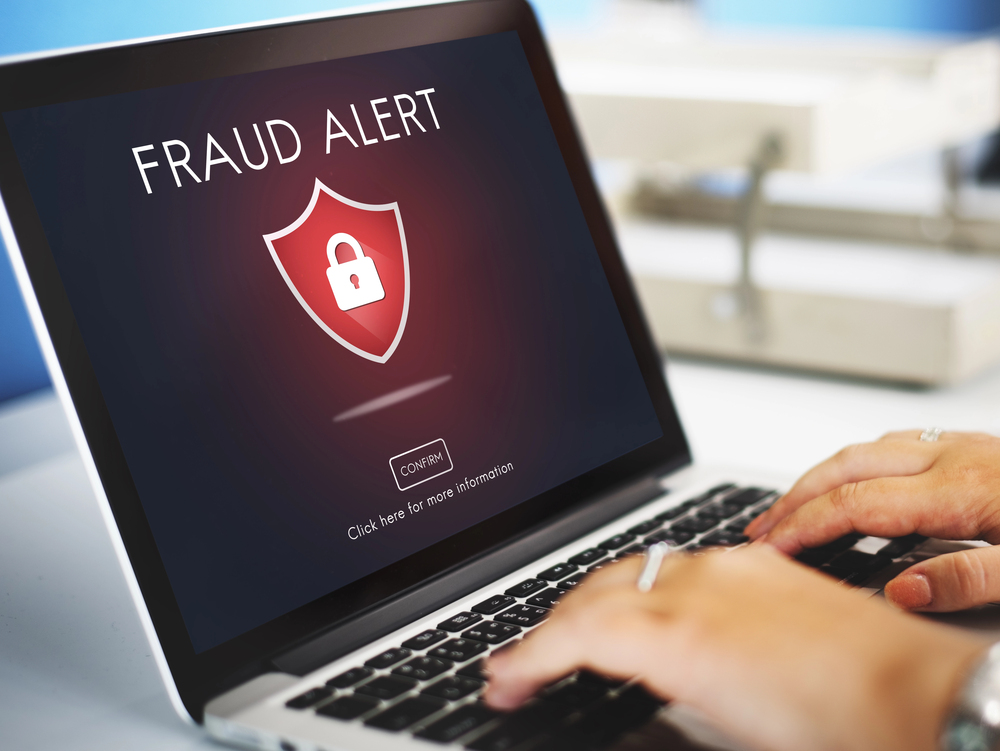 Laptop screen displaying a fraud alert notification with a shield and padlock icon and a confirm button.