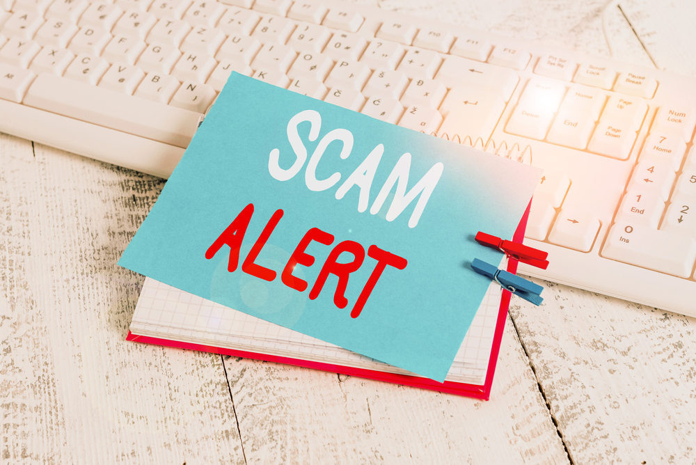A blue note with the words SCAM ALERT written in large letters, attached to a notebook sitting on a computer keyboard.